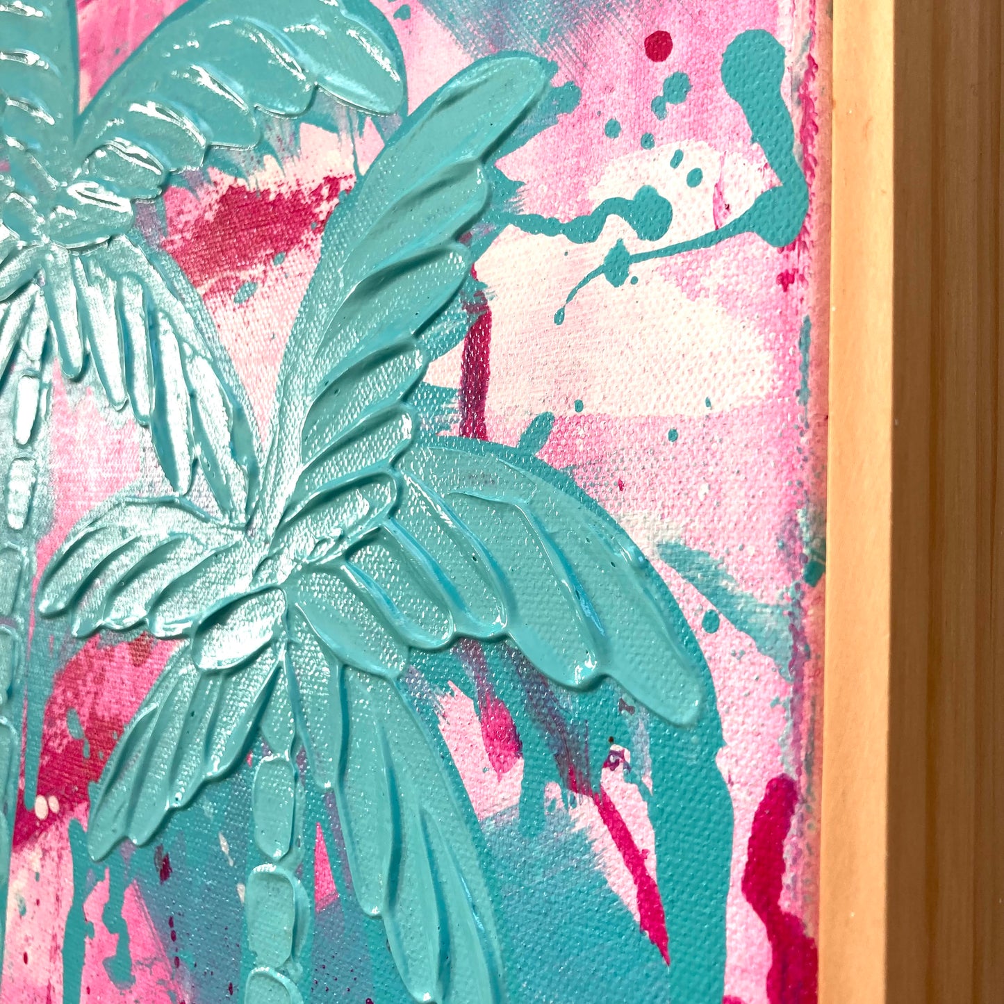 Close up shot of Dreaming Under The Palms showing the texture of the palm trees against an abstract pink and aqua background and also showing the raw pine frame